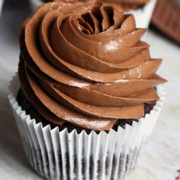 Chocolate Zucchini Cupcakes with Chocolate Frosting in a white paper cupcake liner on a wooden table