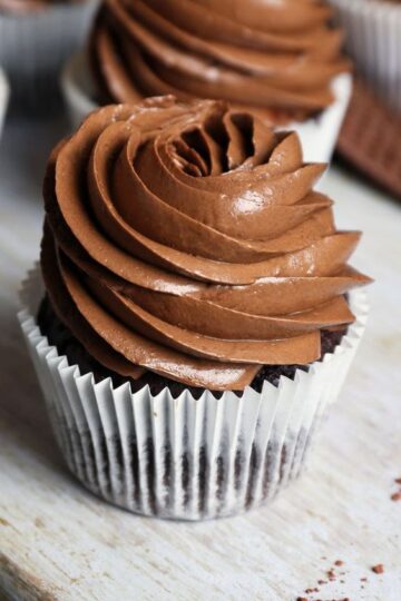 Chocolate Zucchini Cupcakes with Chocolate Frosting in a white paper cupcake liner on a wooden table