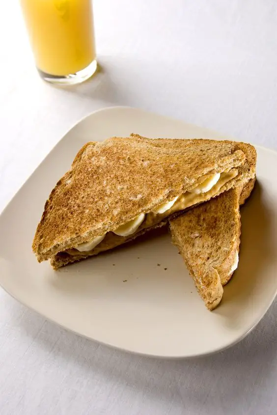 Grilled Banana Peanut Butter Sandwich cut in half diagonally, sitting on a white plate.
