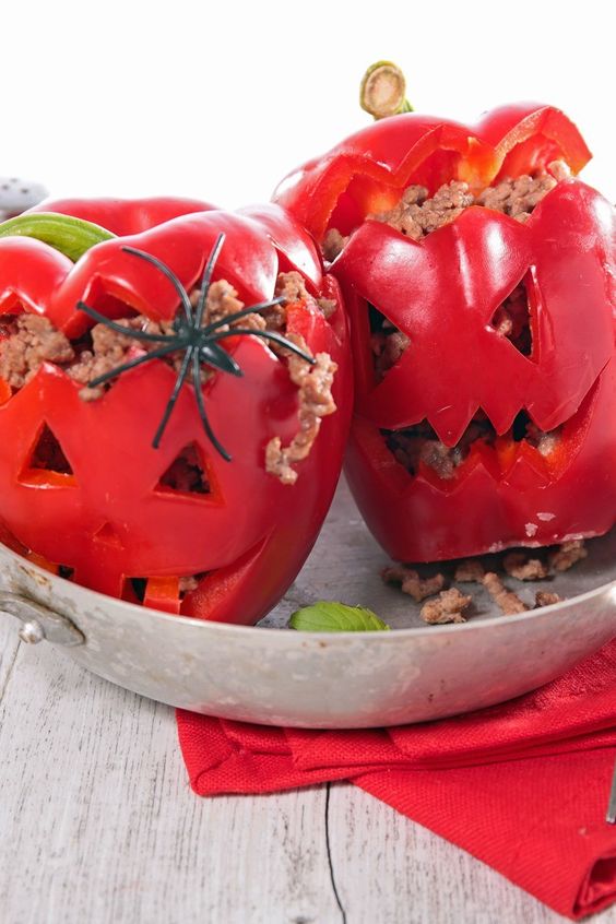Red bell peppers stuffed with ground beef with Halloween Jack-o-lantern faces carved in them. In a metal bowl.