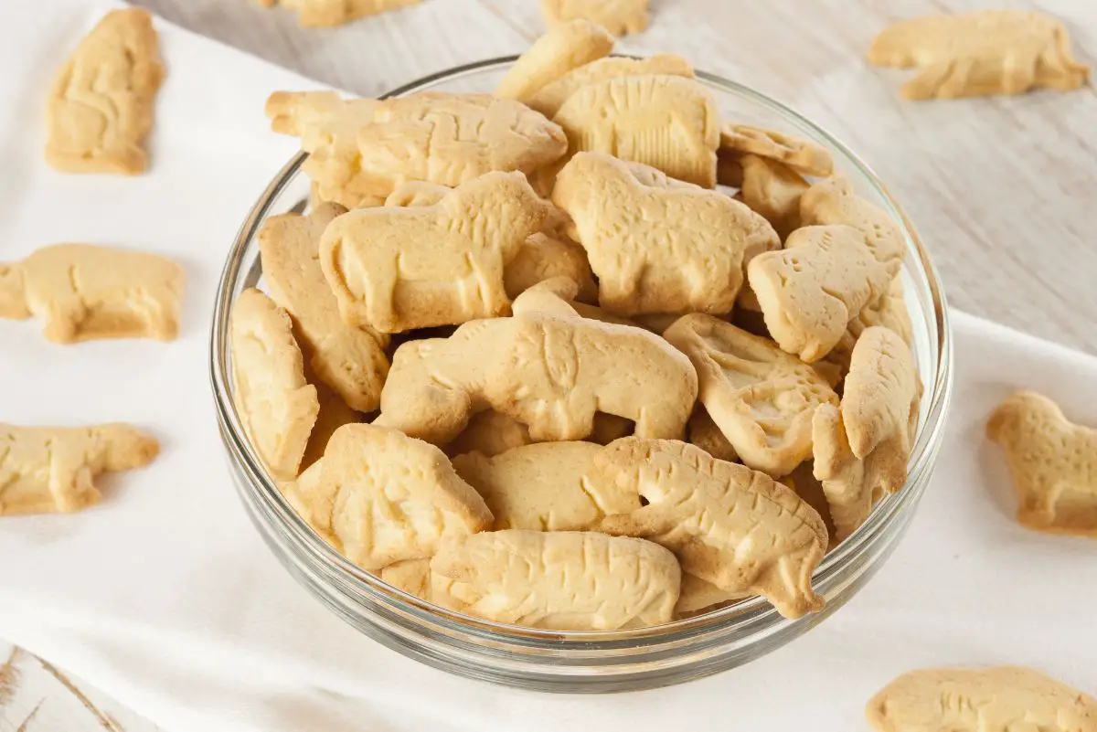 Animal crackers in a clear glass bowl with a few scattered around the bowl.