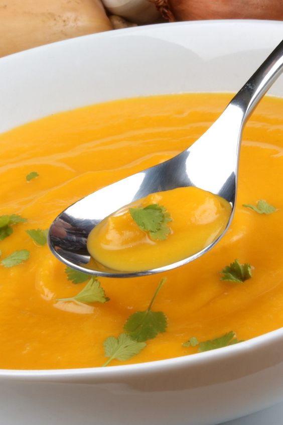 Closeup of Butternut Squash Soup in a white bowl, A spoonful of soup hovering over the bowl.