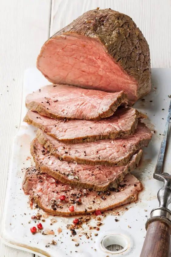 Roast beef half sliced on a white cutting board.