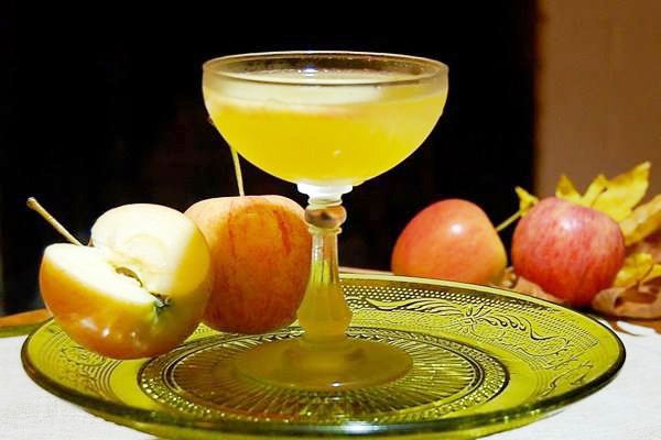 An Apple Cider Vodka Martini on a glass plate with apples and leaf decorations.