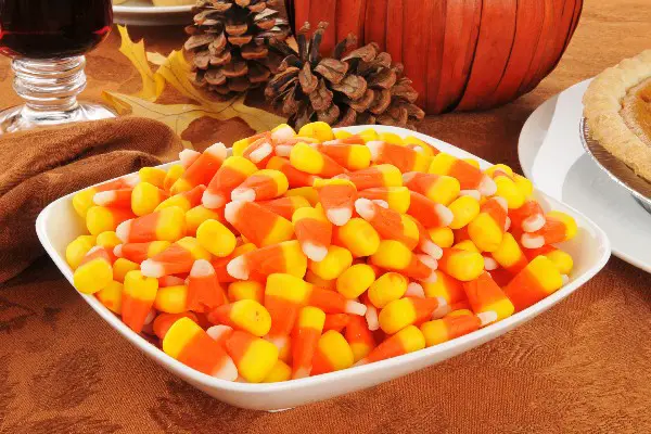Homemade Halloween Candy Corn in a white bowl with pinecones and a pumpkin in the background.