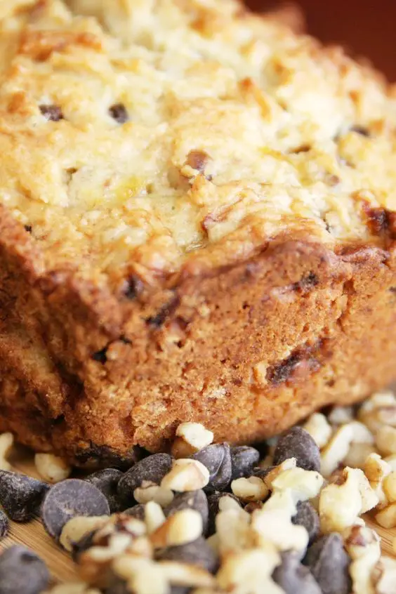 Closeup of zucchini bread surrounded by chocolate chips and chopped walnuts.