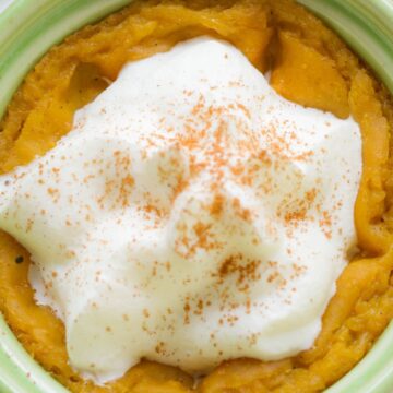 Close-up of crockpot pumpkin spice pudding in a green ramekin, topped with whipped cream and a dusting of cinnamon. The creamy texture and warm spices make it a cozy fall dessert.