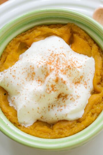 Close-up of crockpot pumpkin spice pudding in a green ramekin, topped with whipped cream and a dusting of cinnamon. The creamy texture and warm spices make it a cozy fall dessert.