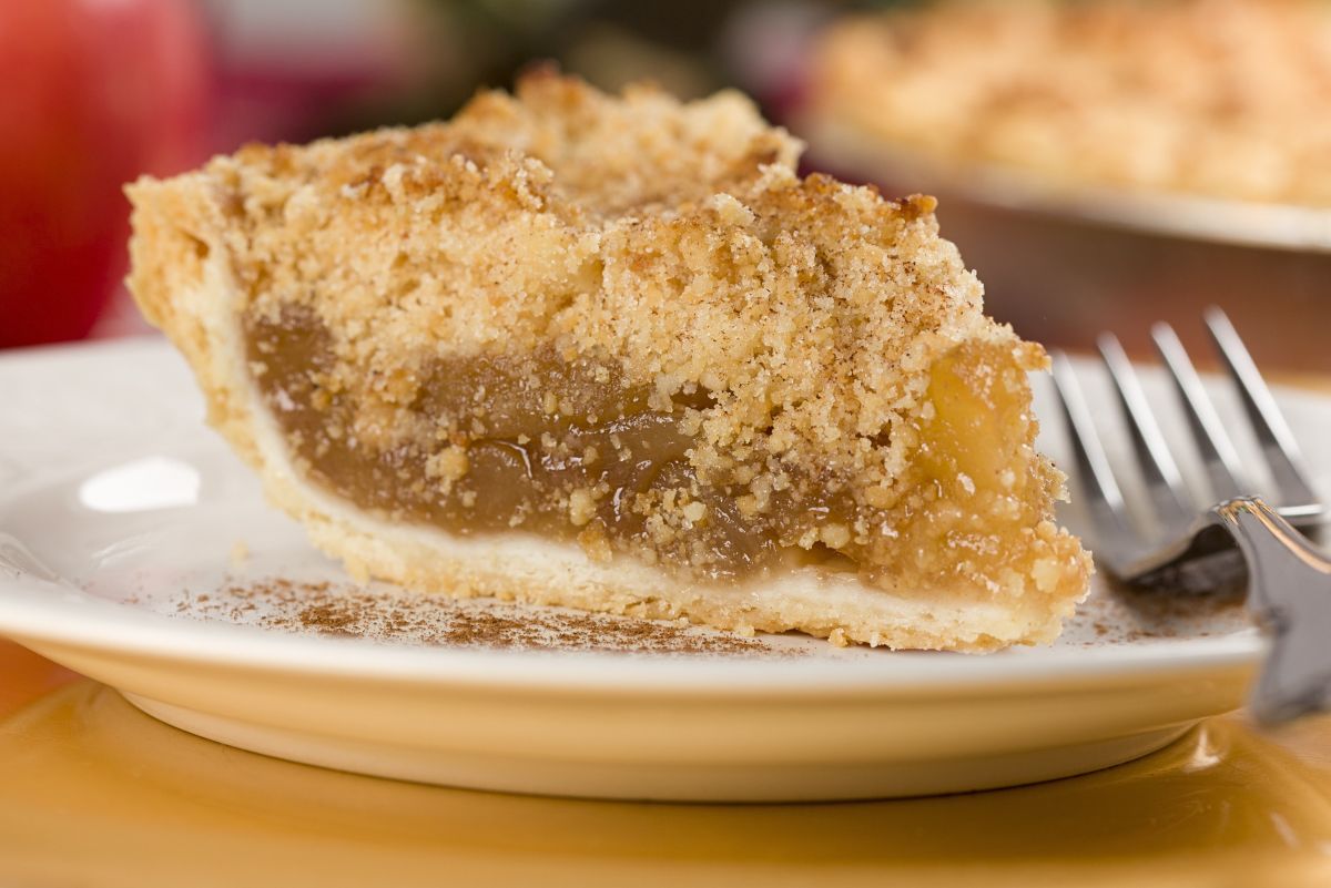 Slice of Granny Smith apple crumb pie on a plate with a fork, featuring a buttery crumb topping, gooey spiced apple filling, and flaky crust dusted with cinnamon.
