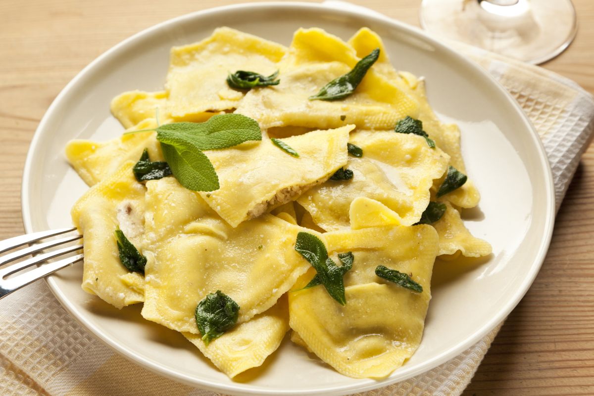 Plate of homemade butternut squash ravioli topped with fresh sage leaves and a light butter sauce. The golden pasta squares have a rustic, hand-cut look, creating a warm and comforting Italian-inspired dish.