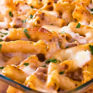 Close-up of a baked Italian macaroni and cheese casserole in a glass dish, with rigatoni pasta coated in creamy melted cheese, browned spots on top, bits of ground meat, and a sprinkle of fresh parsley, classic comfort food pasta bake for dinner.