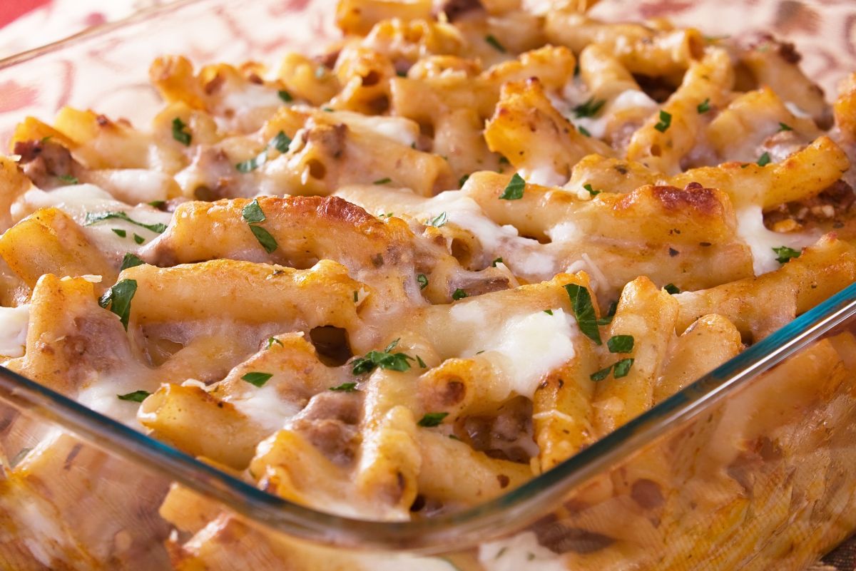 Cheesy Italian macaroni and cheese baked ziti in a glass casserole dish, with ridged pasta tubes coated in golden melted cheese, small bits of ground meat, and parsley sprinkled on top, classic comfort food pasta casserole for an easy weeknight dinner.