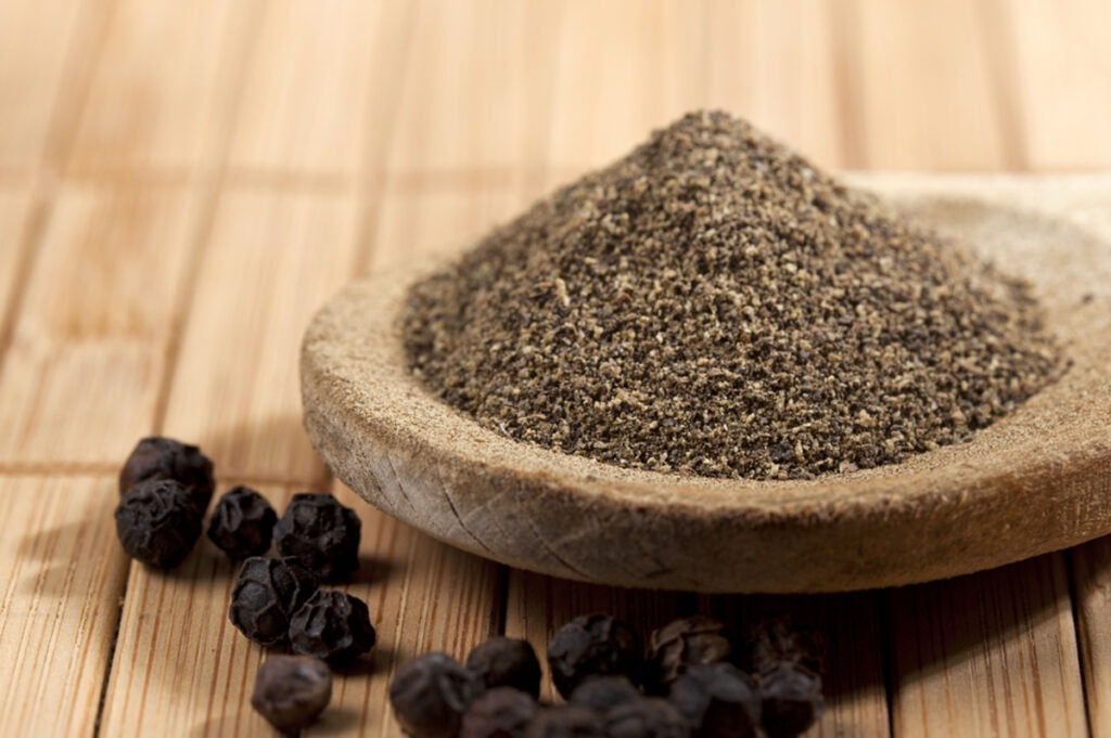 heap of powdered black pepper on a wooden spoon and pepper corns, shallow depth of field.