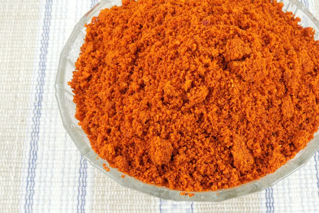 Chili powder in a clear glass bowl, sitting on a light colored cloth.