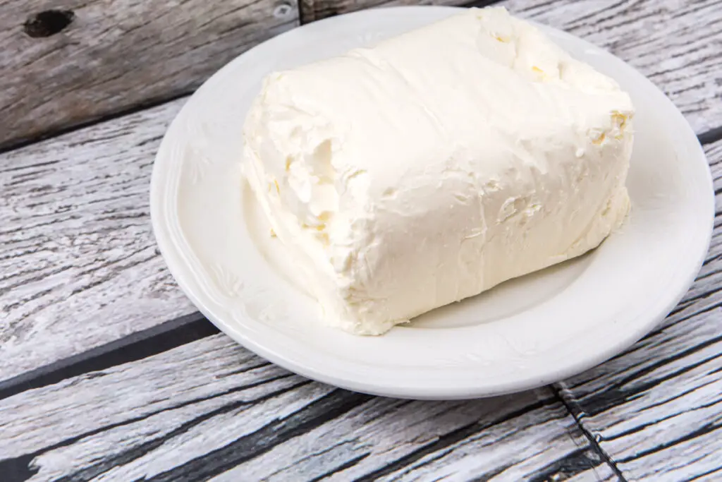 Block of cream cheese on a white plate, sitting on a rustic wooden table.