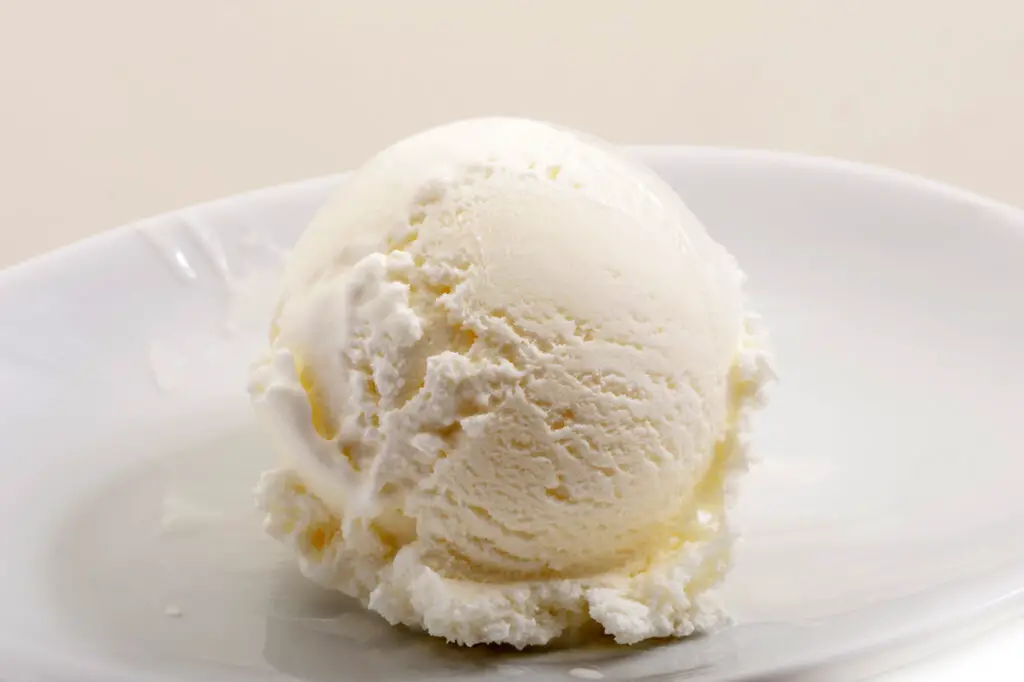 Scoop of vanilla ice cream on a white plate, with a white background.
