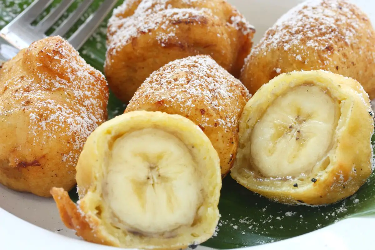 Banana Fritters in a bowl. One fritter is cut in half showing the banana inside.