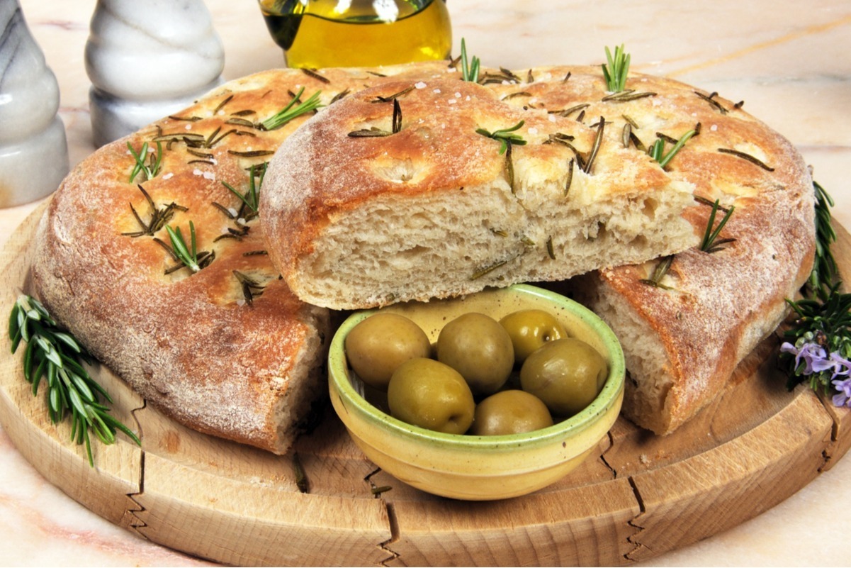 Copycat Macaroni Grill Rosemary Bread on a wooden cutting board with a small green dish of olives next to it.