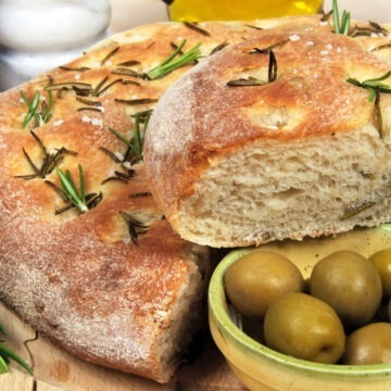 Copycat Rosemary Bread on a cutting board with a small dish of olives.