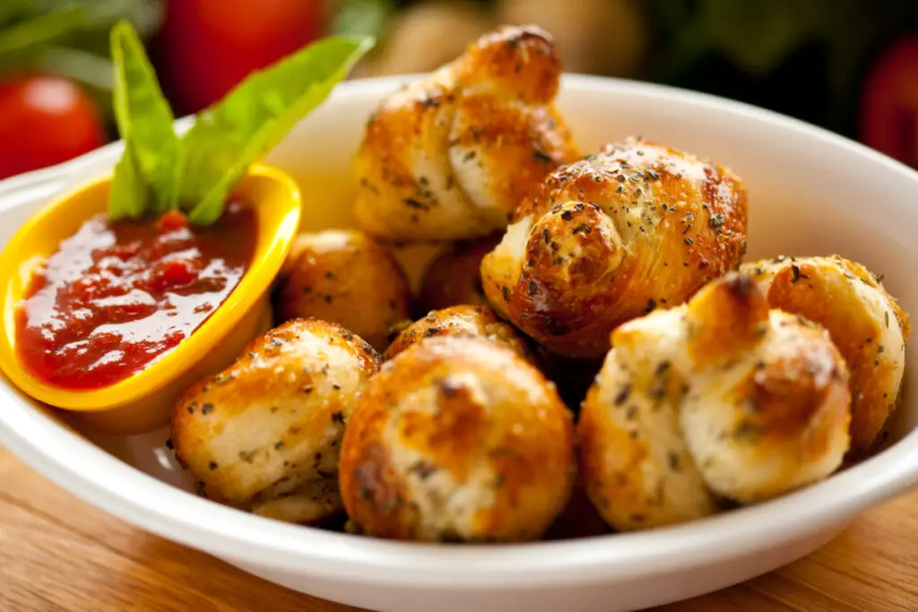 Garlic Knots in a white bowl with marinara sauce on the side.