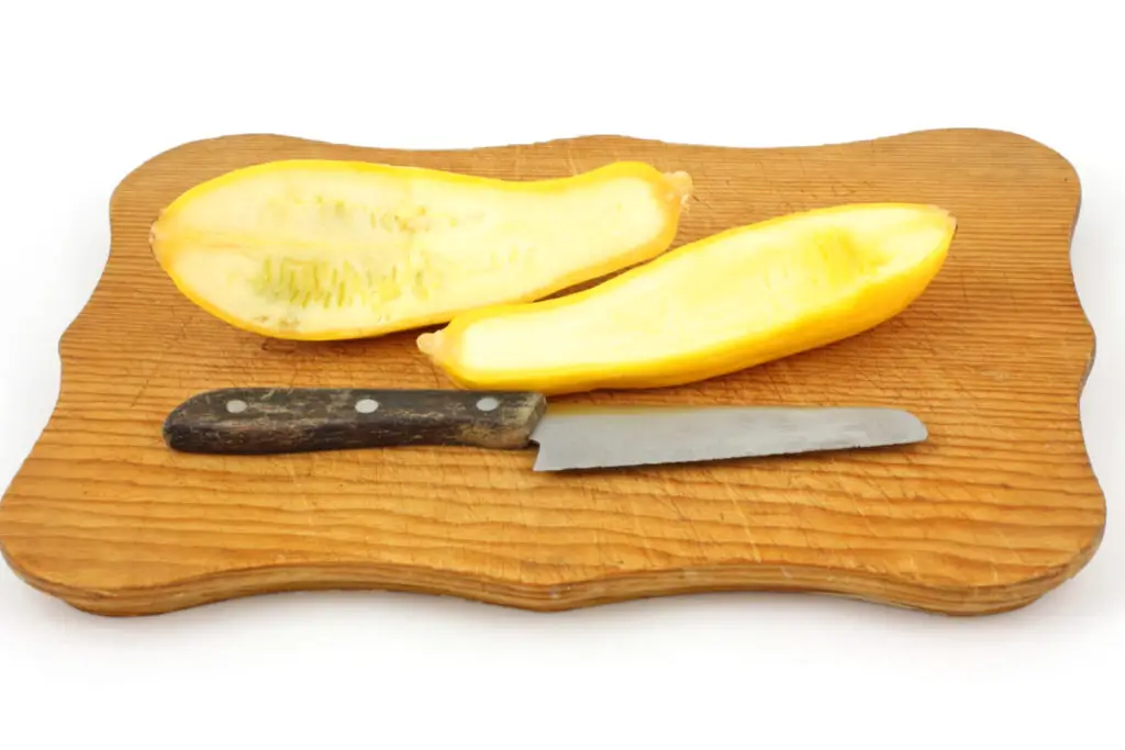 Sliced summer squash on a cutting board with a knife.