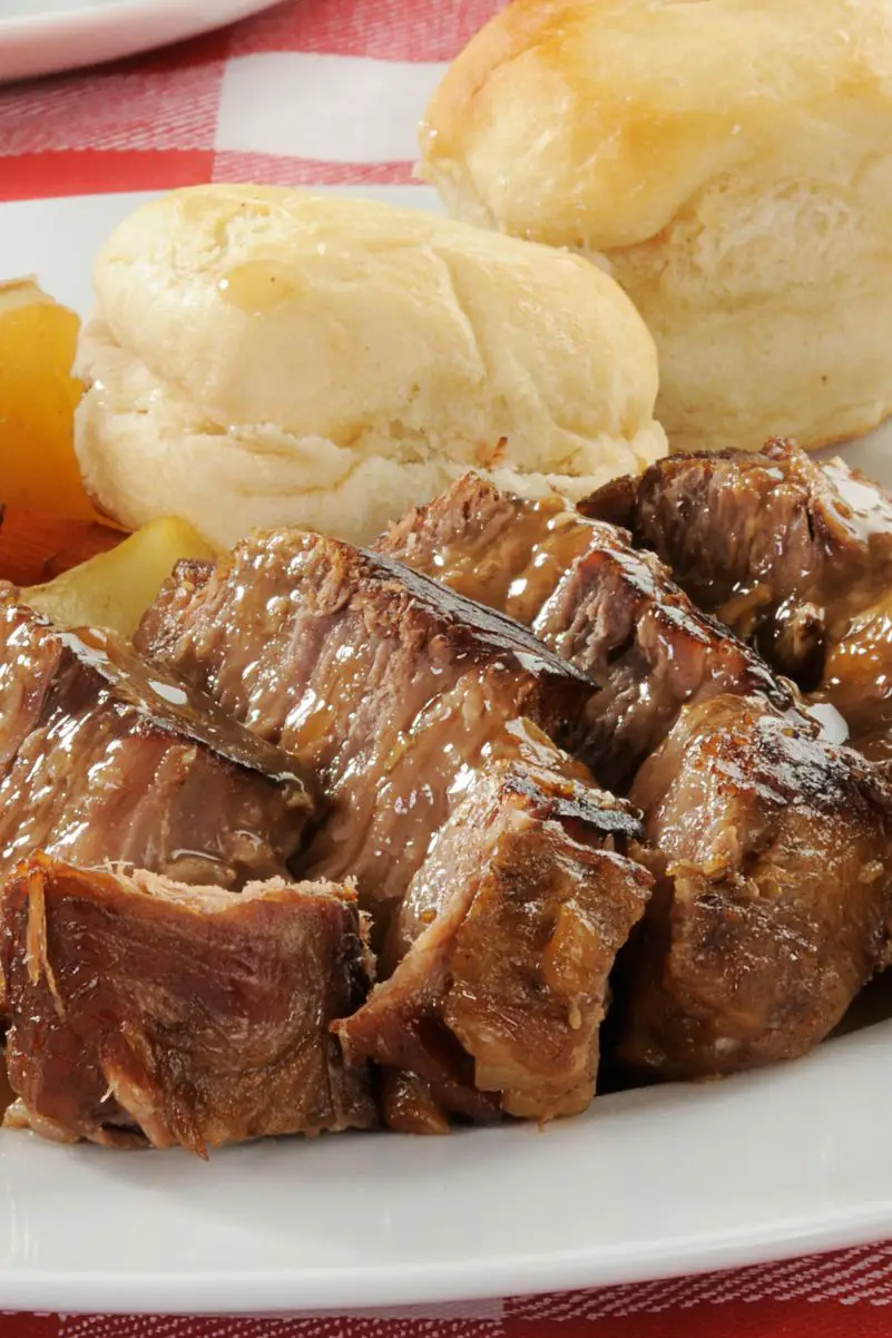 Closeup of Easy Slow Cooker Pot Roast on a white plate with a dinner roll in the background.
