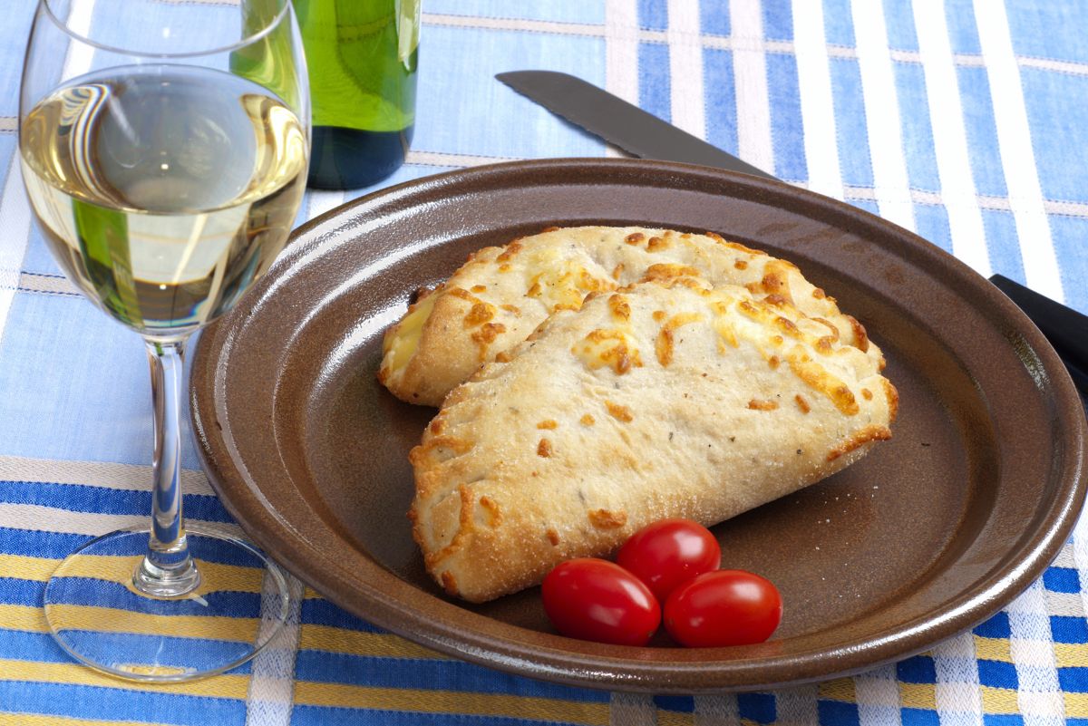 2 Barbecue Chicken Calzones on a brown plate with 3 cherry tomatoes. The plate is on a blue and white striped cloth. A glass of white wine next to the plate.