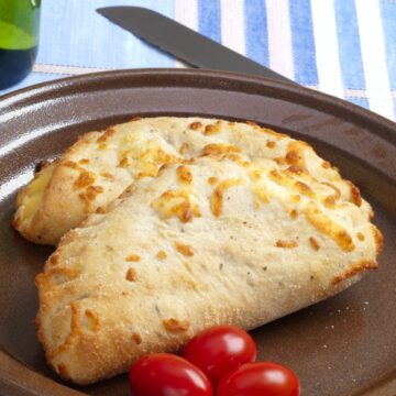 Closeup of 2 Barbecue Chicken Calzones on a brown plate with 3 cherry tomatoes.