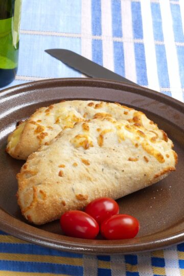 Closeup of 2 Barbecue Chicken Calzones on a brown plate with 3 cherry tomatoes.