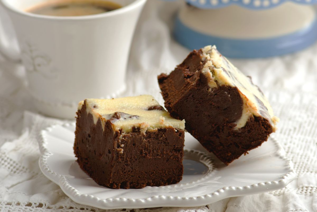 2 Luxurious Bailey's Irish Cream Infused Brownies on a white plate with a cup of coffee behind it.