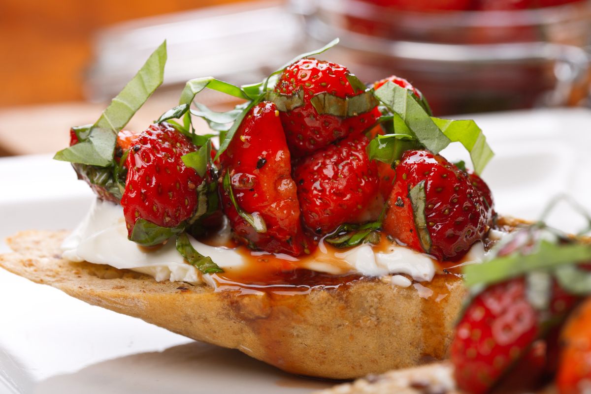 Delicious Strawberry & Goat Cheese Bruschetta on a white surface with fresh strawberries in front of it.