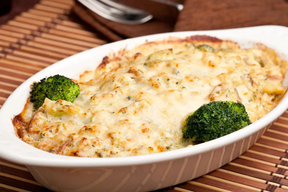 Ultimate Broccoli Mushroom and Cheddar Casserole in a white casserole dish on a brown place mat.