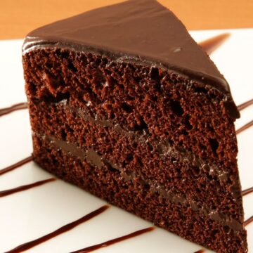 Closeup of a slice of Sinfully Delicious Coffee and Chocolate Cake on a white plate with chocolate drizzle.