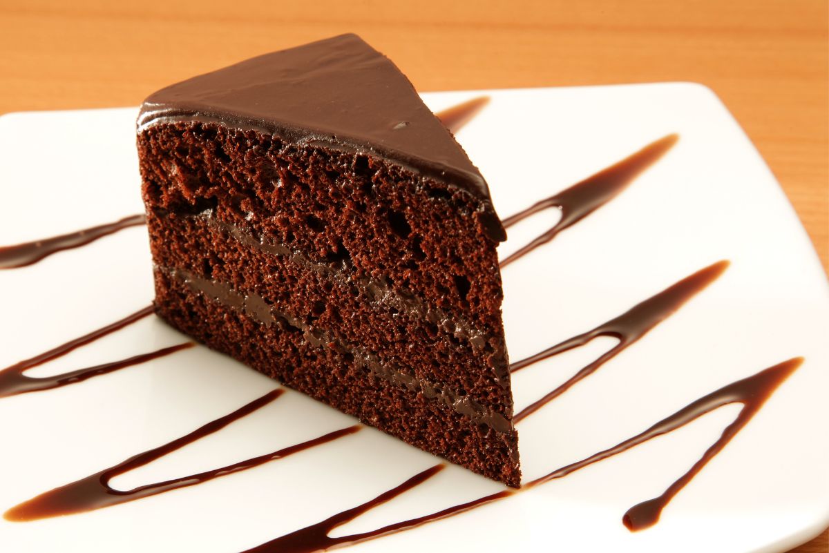 A slice of Sinfully Delicious Coffee and Chocolate Cake on a square, white plate with chocolate sauce zig zags across it.