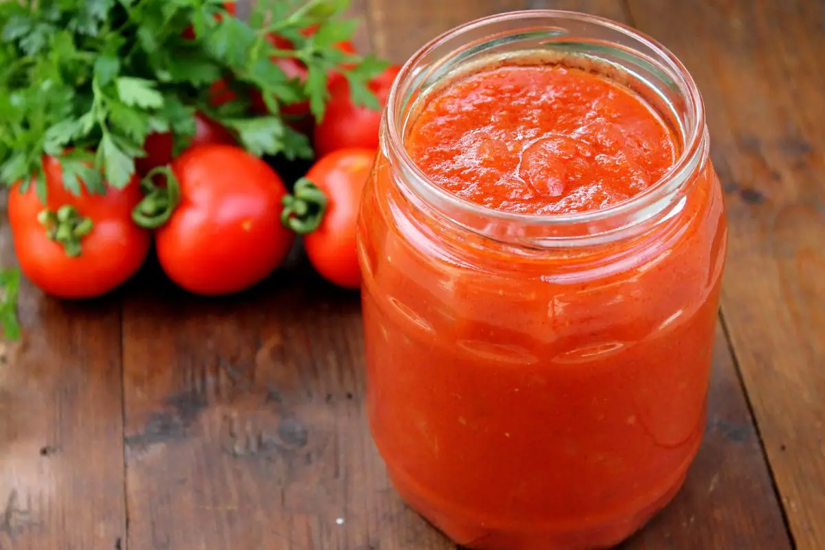 Pizza Sauce n a clear glass jar with fresh tomatoes behind it.