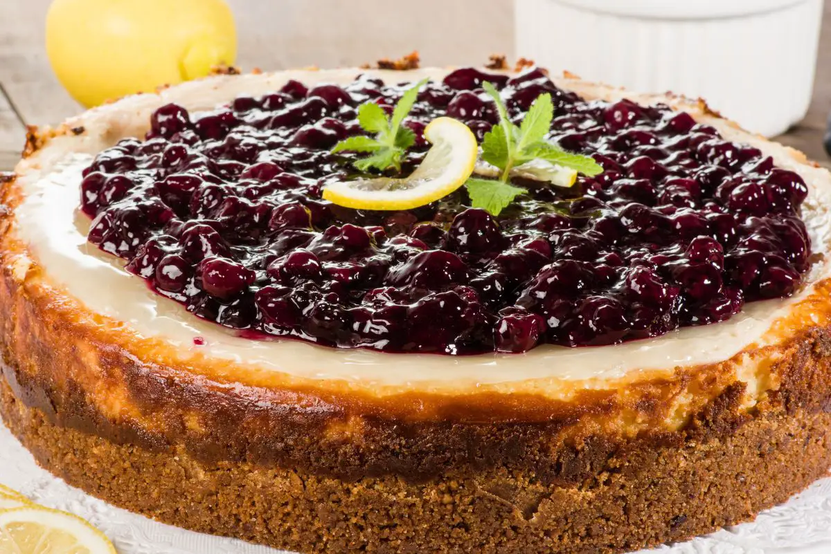 Best Lemon Cheesecake with Blueberries with lemons behind it.