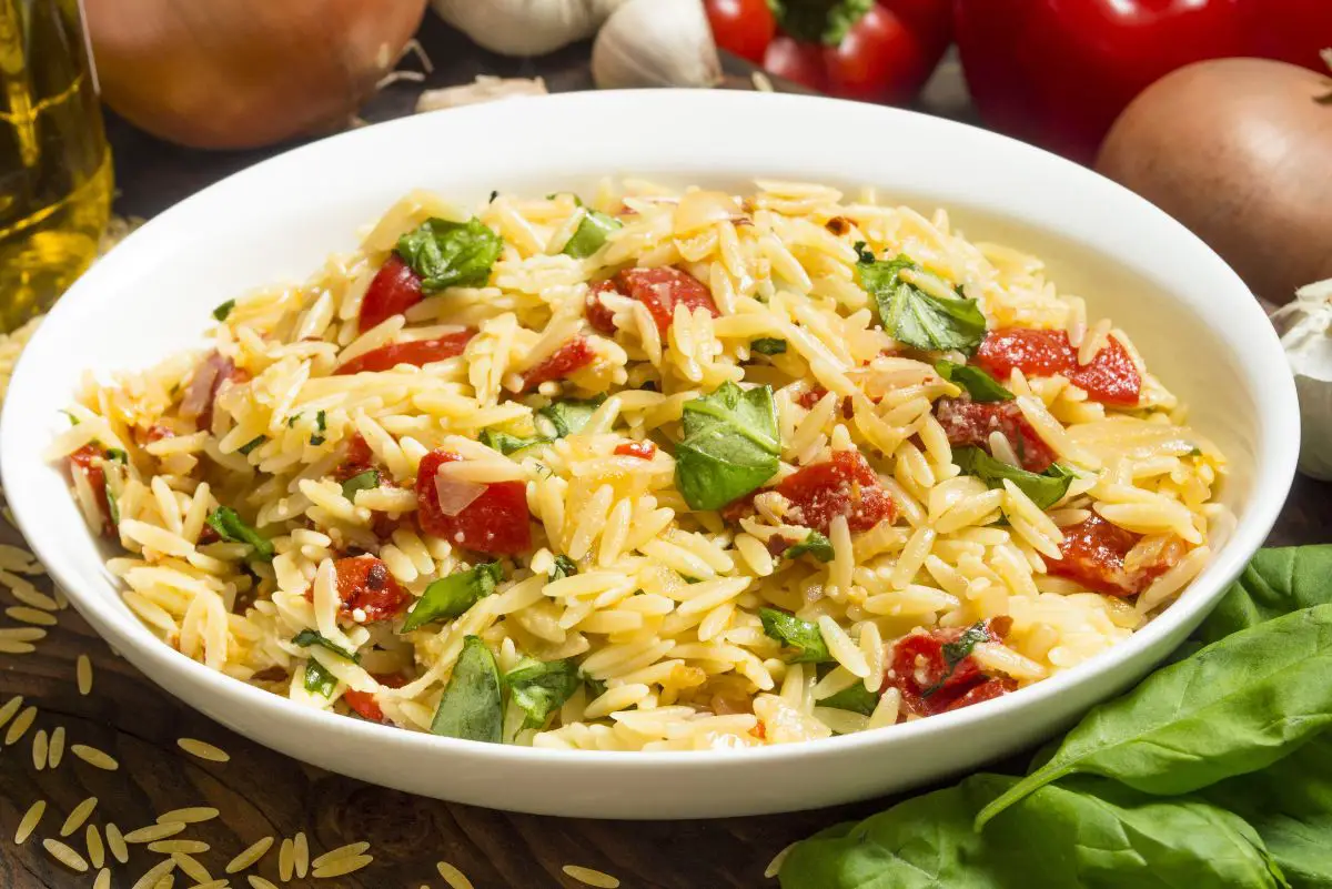 Orzo Pasta Salad with Basil and Tomato in a white bowl with ingredients behind it.