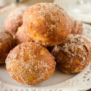 A pile of Homemade Fried Applesauce Doughnuts on a white plate.