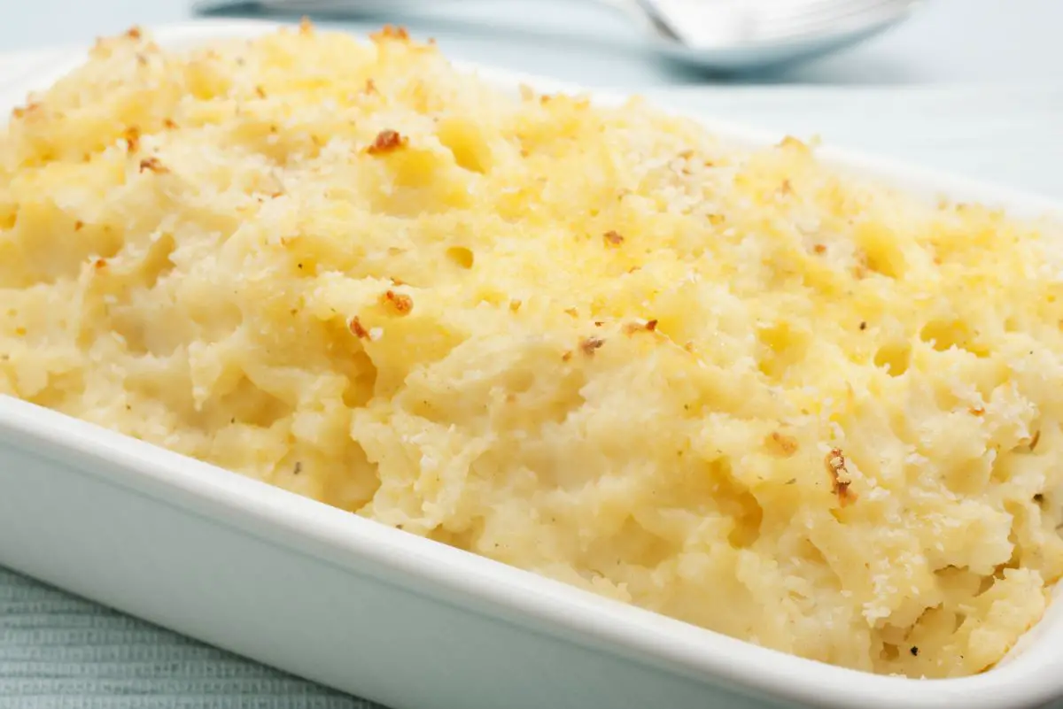 Baked Parmesan Mashed Potatoes in a white ceramic baking dish with a spoon in the background.