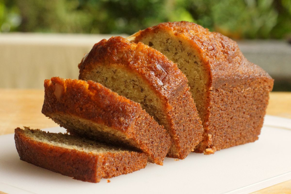 A loaf of Best Banana Bread (Without Nuts) half sliced on a white surface.