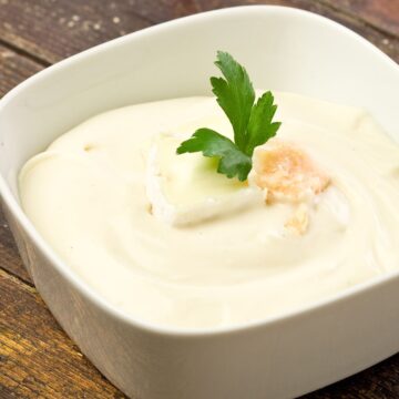 Closeup of Copycat Olive Garden Alfredo Sauce in a white, bowl on a rustic wooden surface.