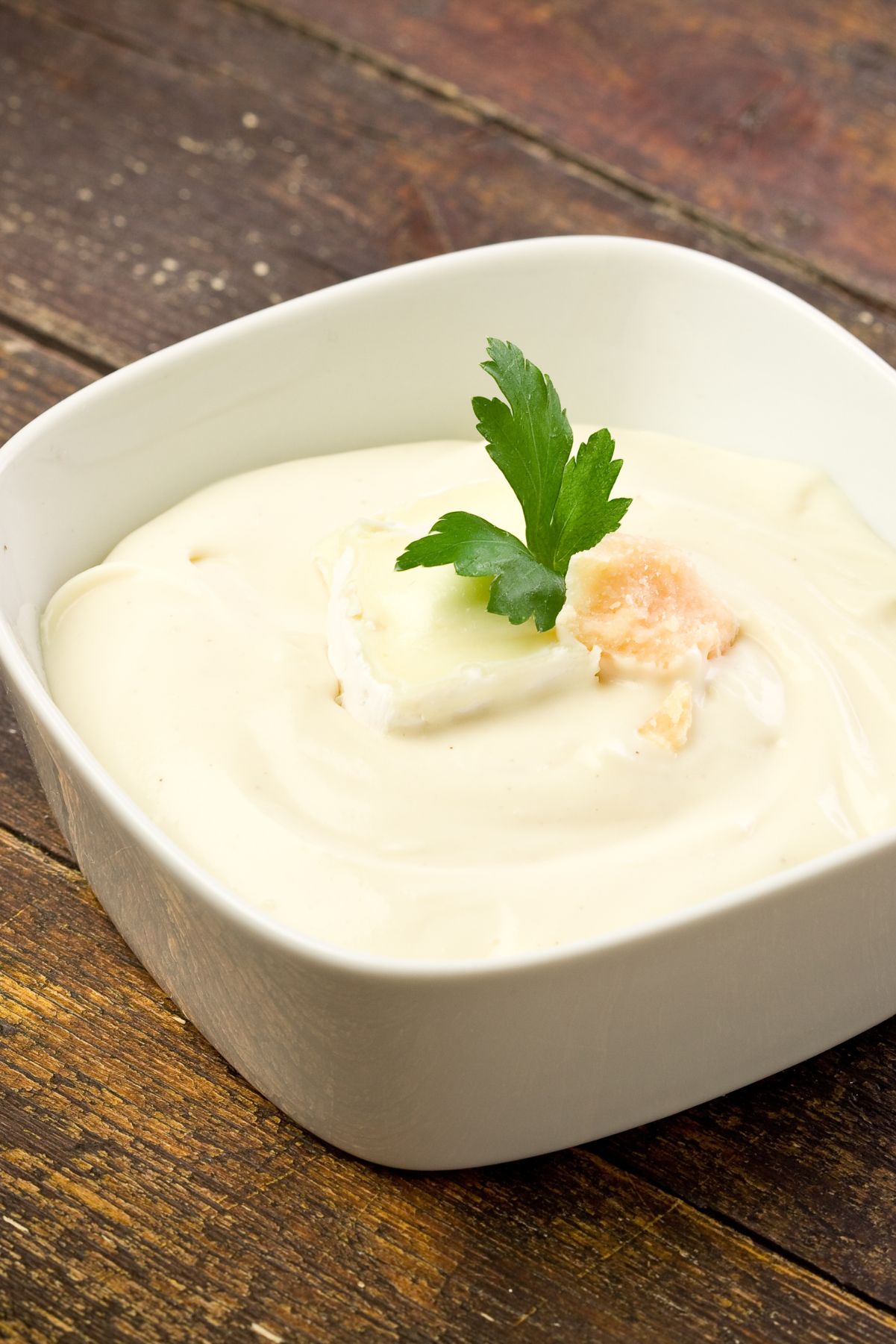 Closeup of Copycat Olive Garden Alfredo Sauce in a white, bowl on a rustic wooden surface.