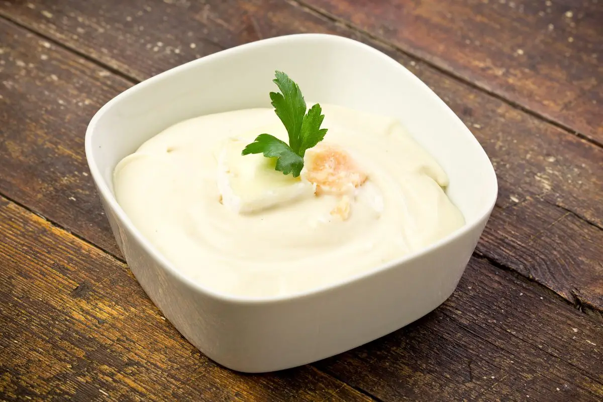Copycat Olive Garden Alfredo Sauce in a square, white bowl sitting on a dark, wooden surface.