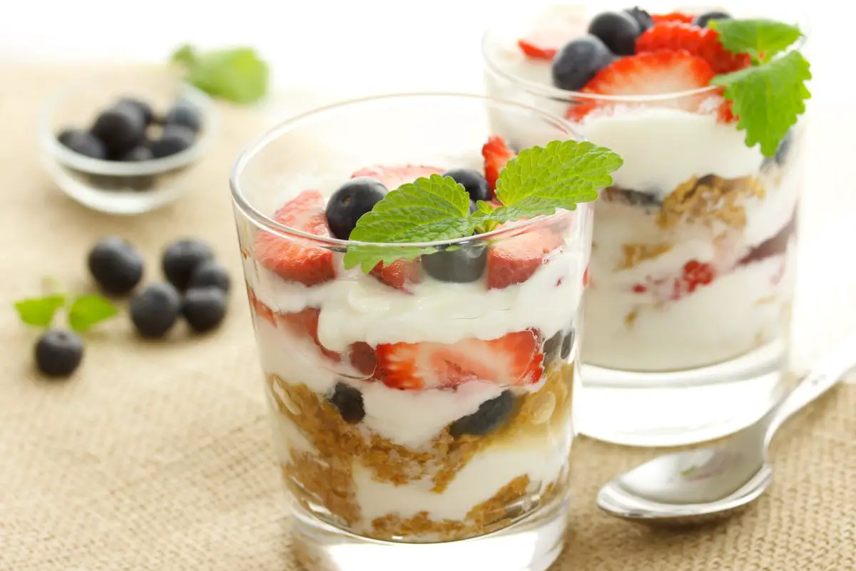 2 Easy Mixed Berry Yogurt Parfaits in clear glasses with fresh blueberries on the table.