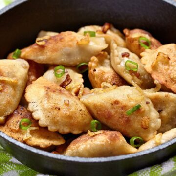 Potato and Cheese Pierogis in a cast iron skillet, sitting on a green and white kitchen towel.