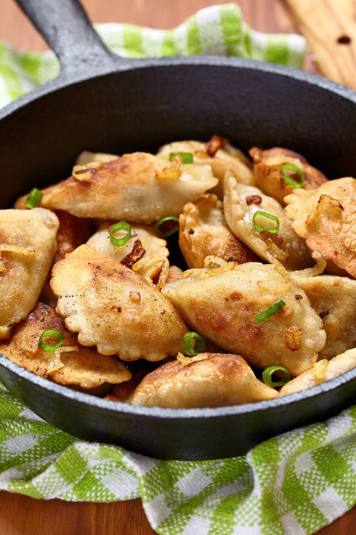 Potato and Cheese Pierogis in a cast iron skillet, sitting on a green and white kitchen towel.