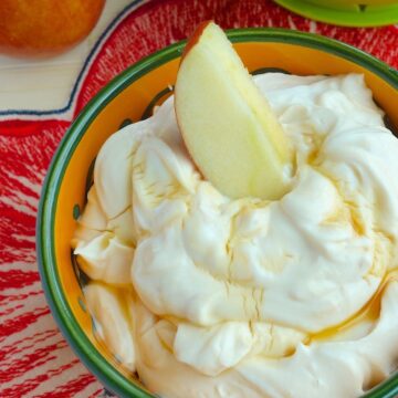 Honey Peanut Butter Greek Yogurt Dip in an orange and green bowl with an apple slice in it. A whole apple next to it.