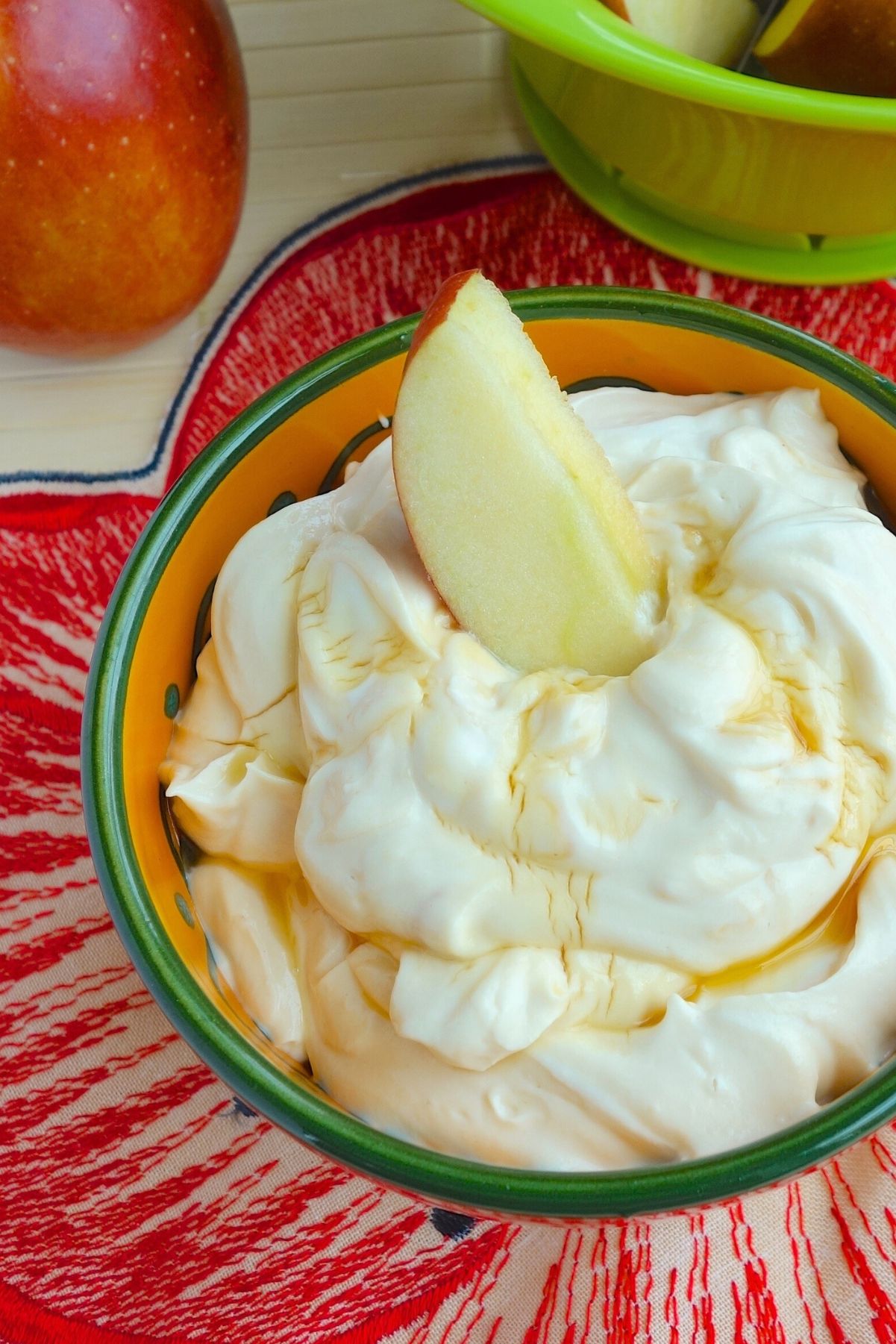 Honey Peanut Butter Greek Yogurt Dip in an orange and green bowl with an apple slice in it. A whole apple next to it.