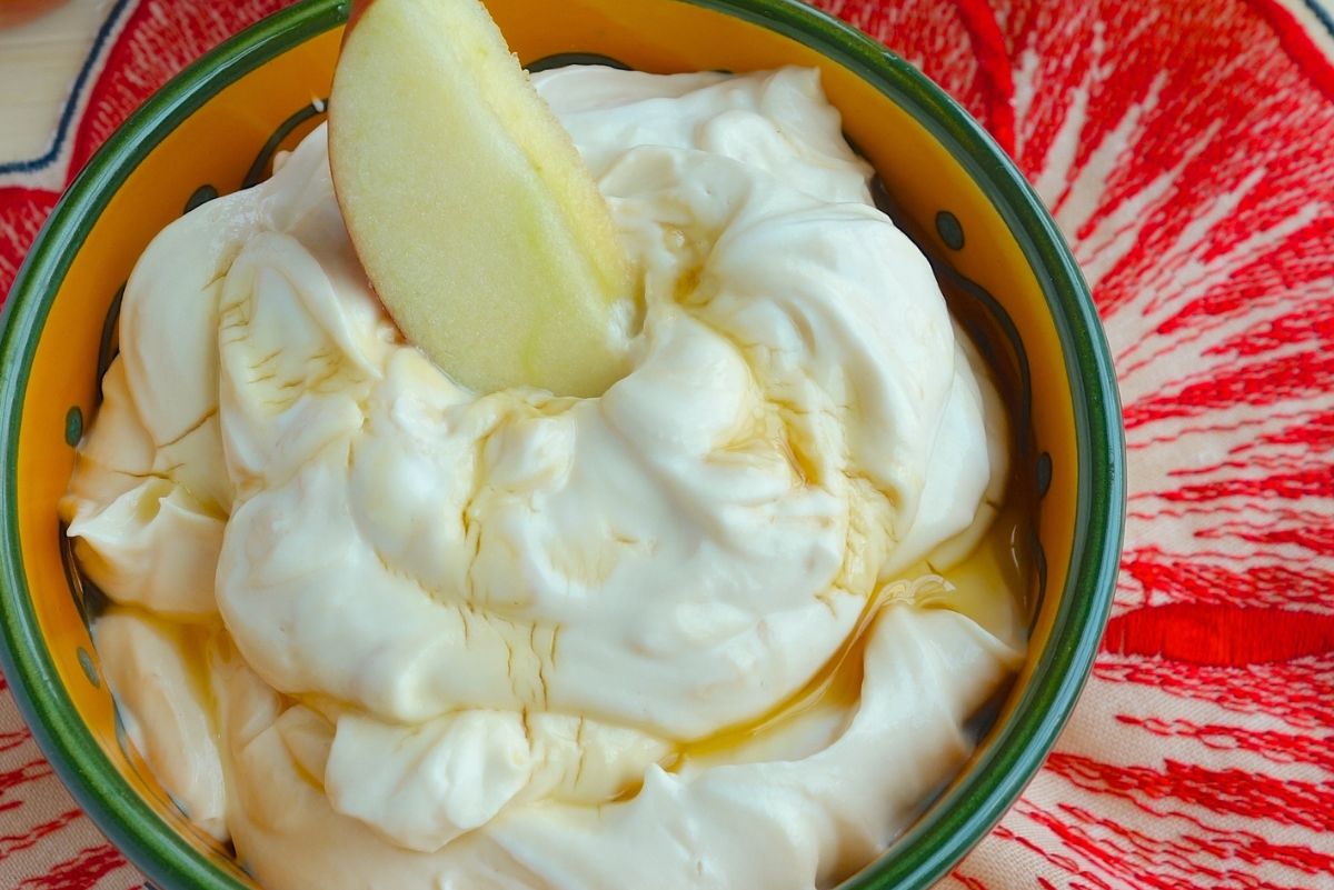 Closeup of Irresistible Honey Peanut Butter Greek Yogurt Dip in an orange and green bowl with an apple slice in it.