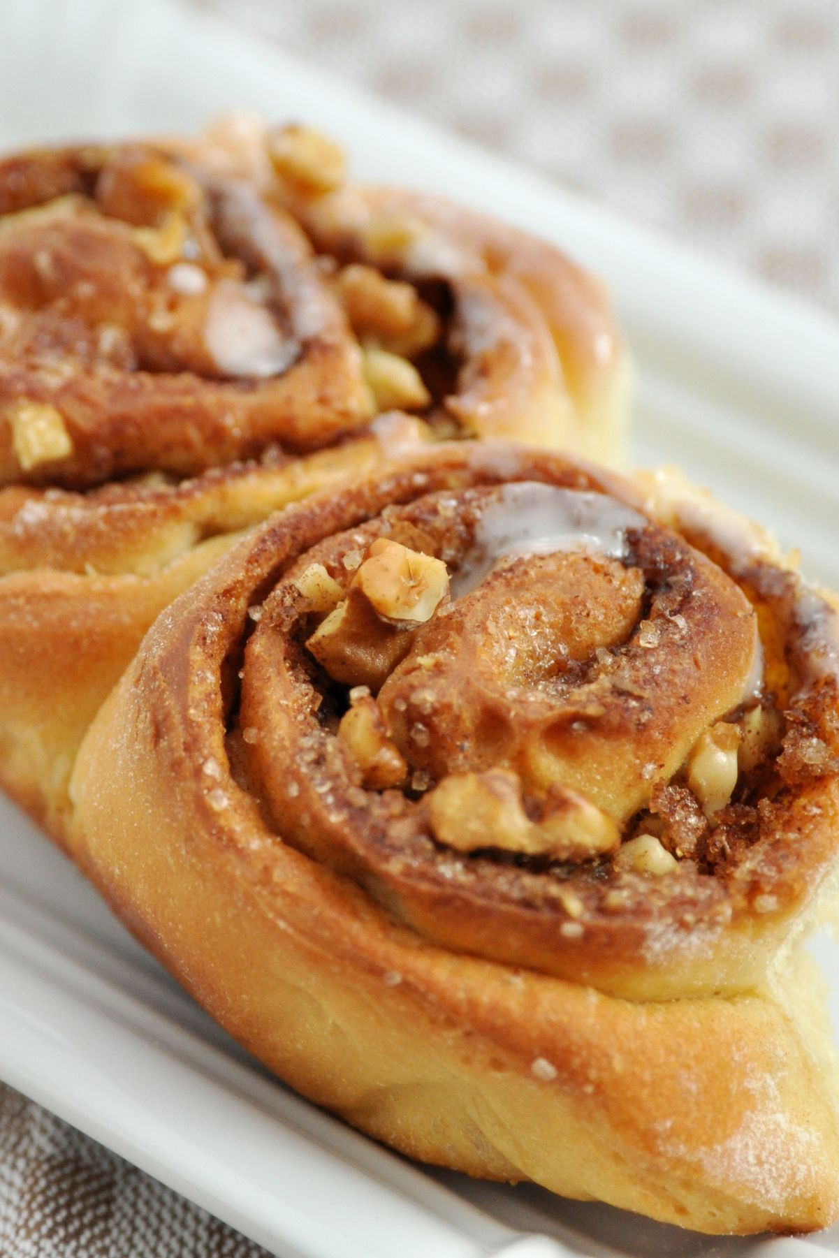 Closeup of 2 Mouthwatering Homemade Cinnamon Buns on a white surface.